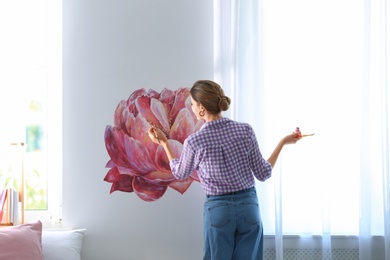 Young interior designer painting flower on wall in modern room