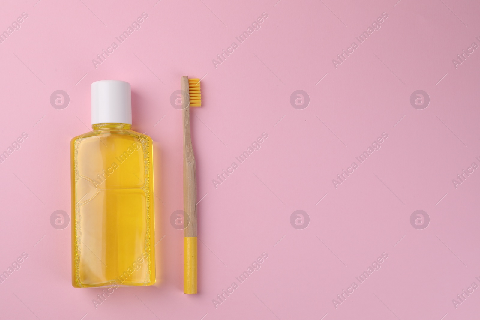 Photo of Fresh mouthwash in bottle and toothbrush on pink background, top view. Space for text