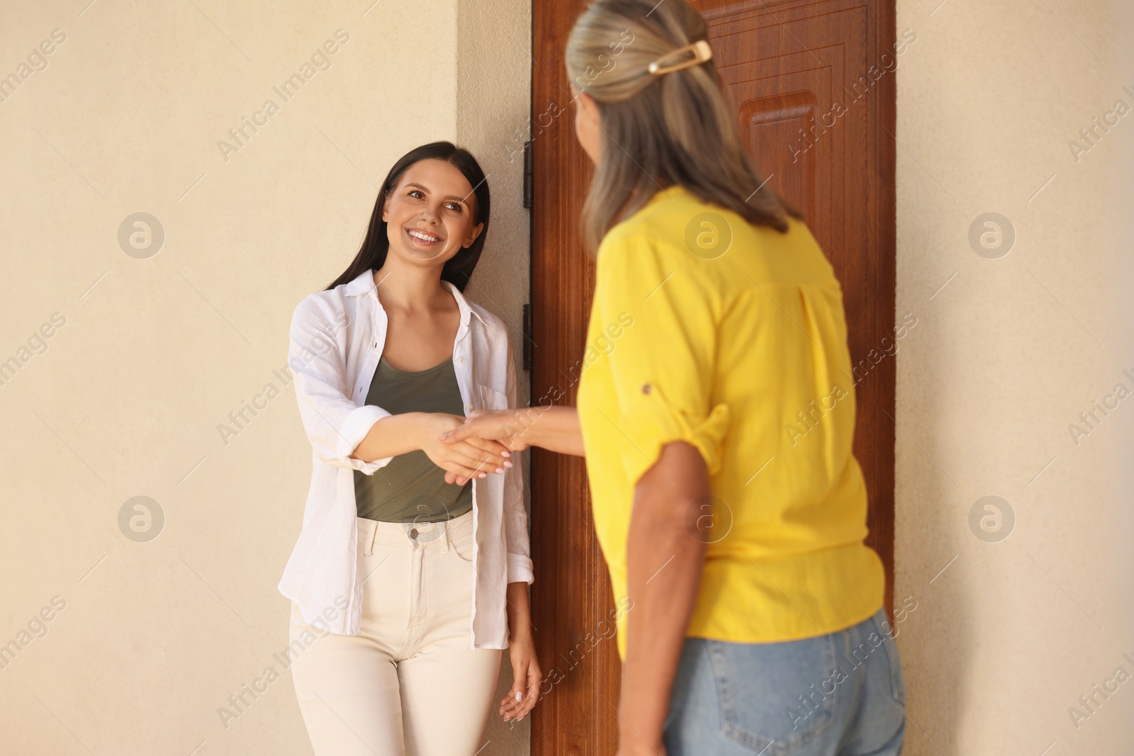 Photo of Friendly relationship with neighbours. Happy women shaking hands near house outdoors