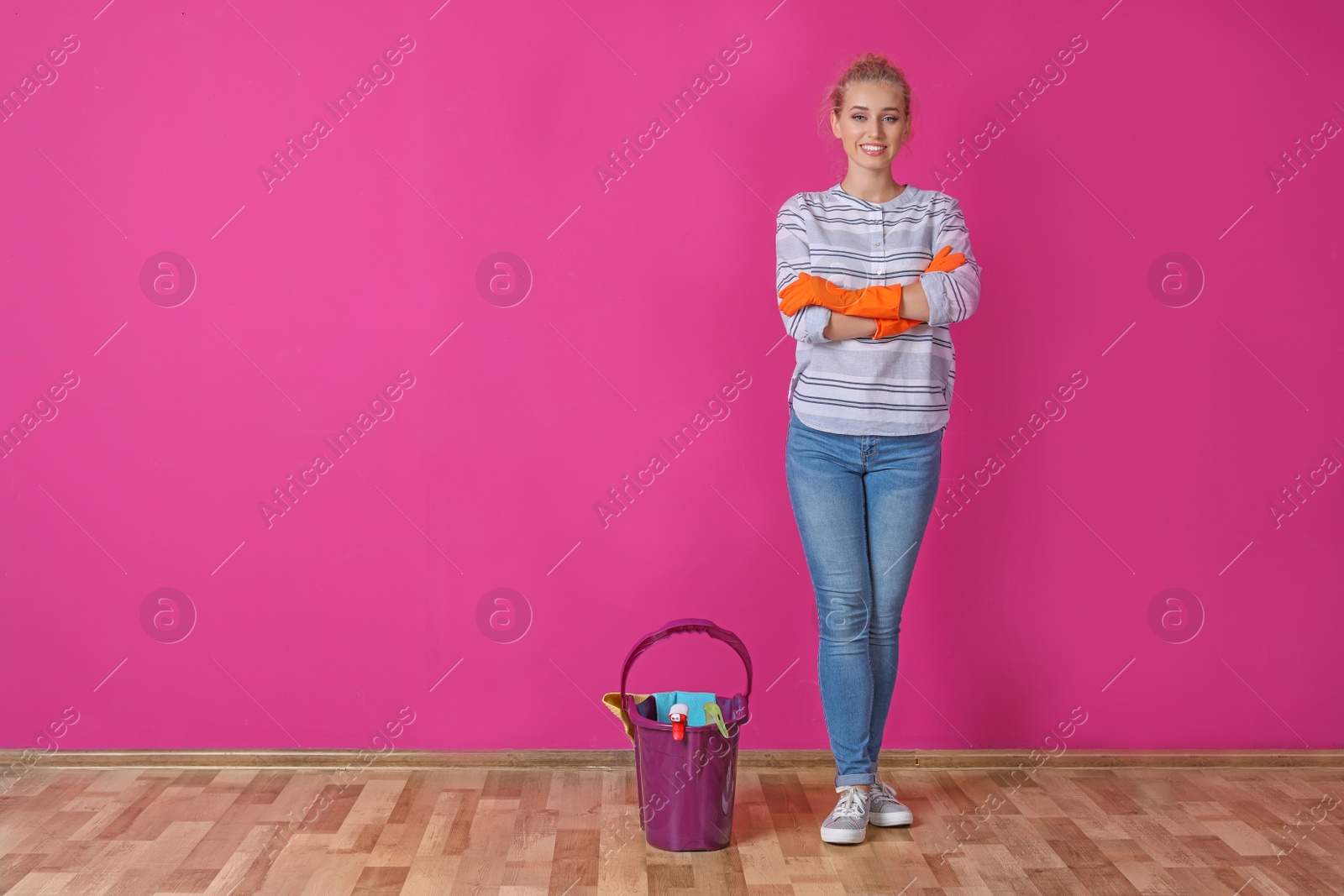 Photo of Woman with cleaning supplies near color wall