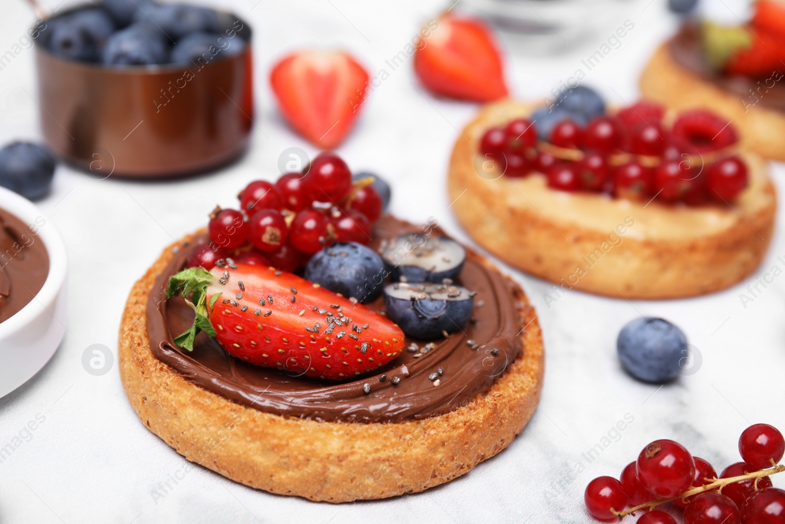 Photo of Tasty organic rusks with different toppings and ingredients on white table, closeup