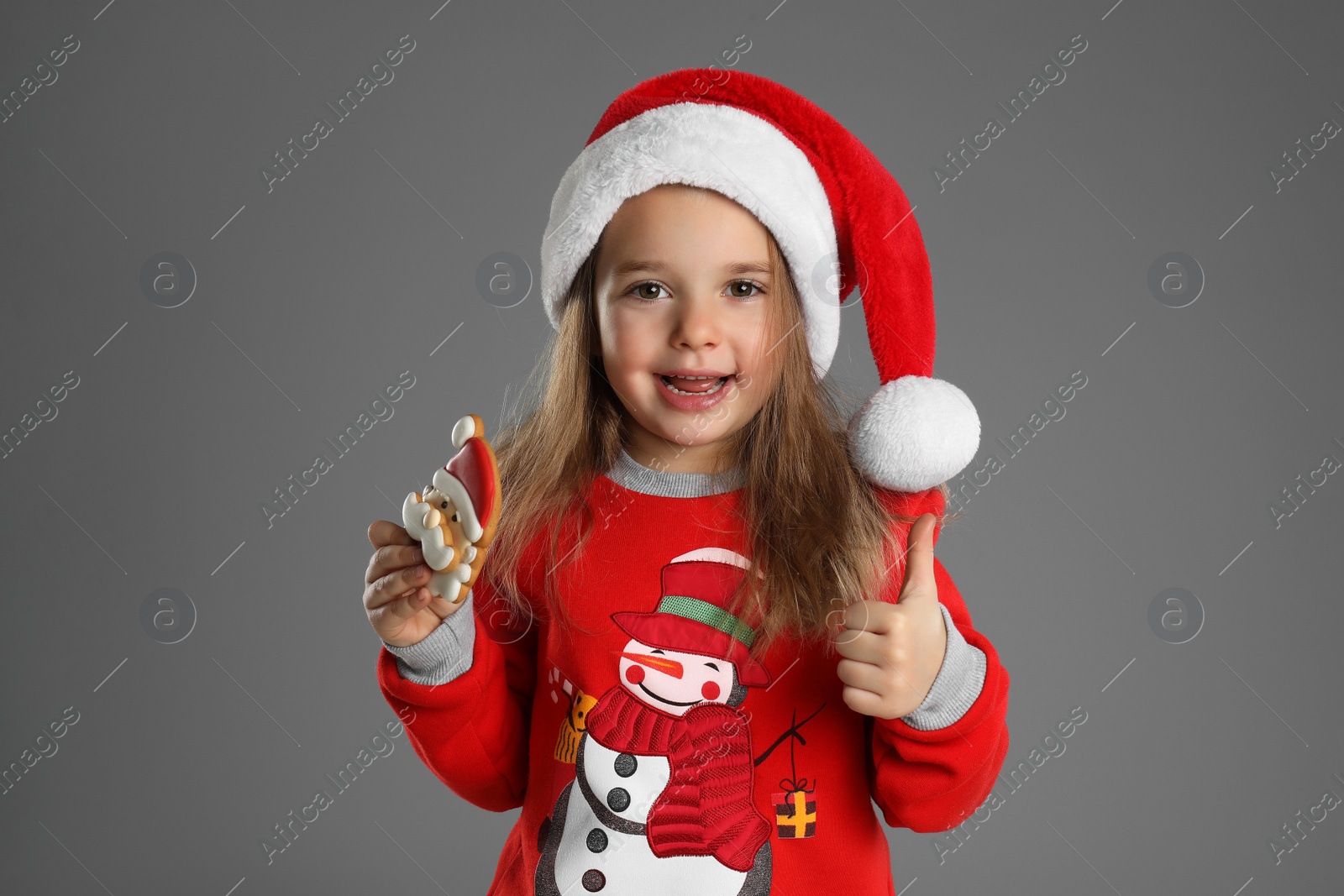 Photo of Cute little girl with Christmas gingerbread cookie on grey background