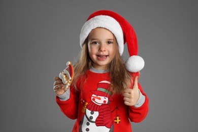 Cute little girl with Christmas gingerbread cookie on grey background