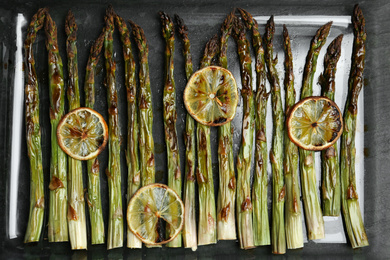 Photo of Oven baked asparagus with lemon slices in glass dish on table, flat lay