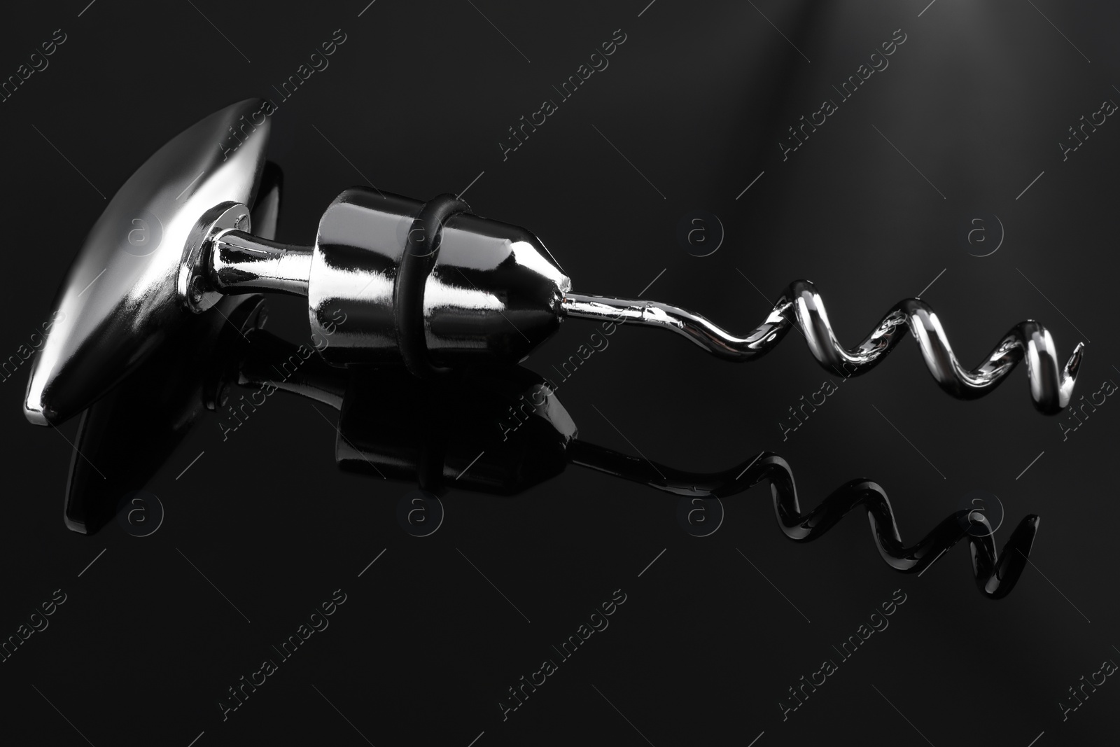 Photo of One metal corkscrew on dark mirror surface, closeup