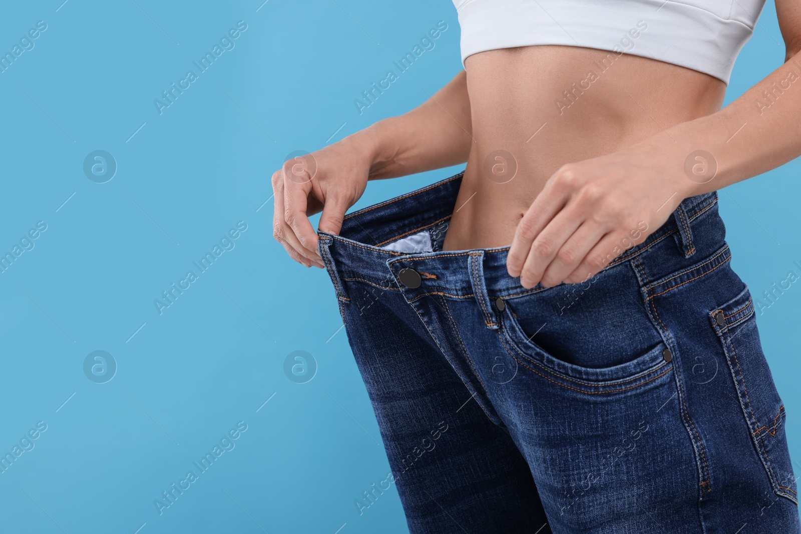 Photo of Slim woman wearing big jeans on light blue background, closeup and space for text. Weight loss