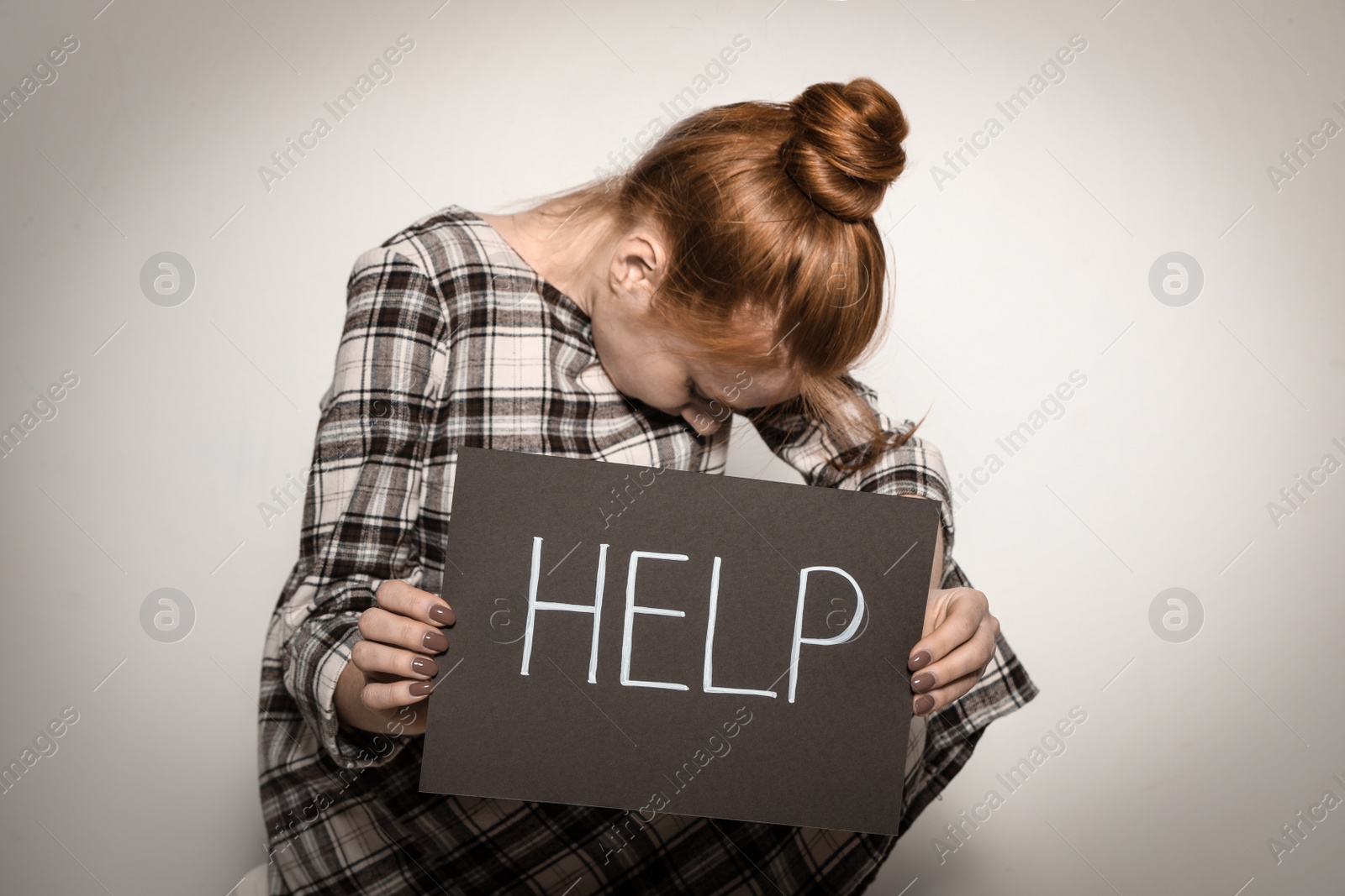 Photo of Young woman holding card with word HELP against light background