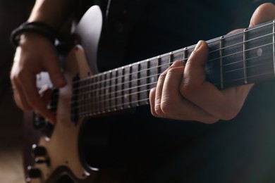 Man playing electric guitar on blurred background, closeup. Rock music