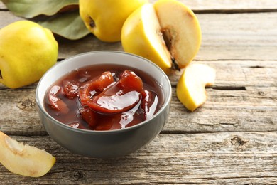 Tasty homemade quince jam in bowl and fruits on wooden table, closeup
