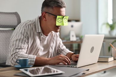 Photo of Man with fake eyes painted on sticky notes using laptop in office