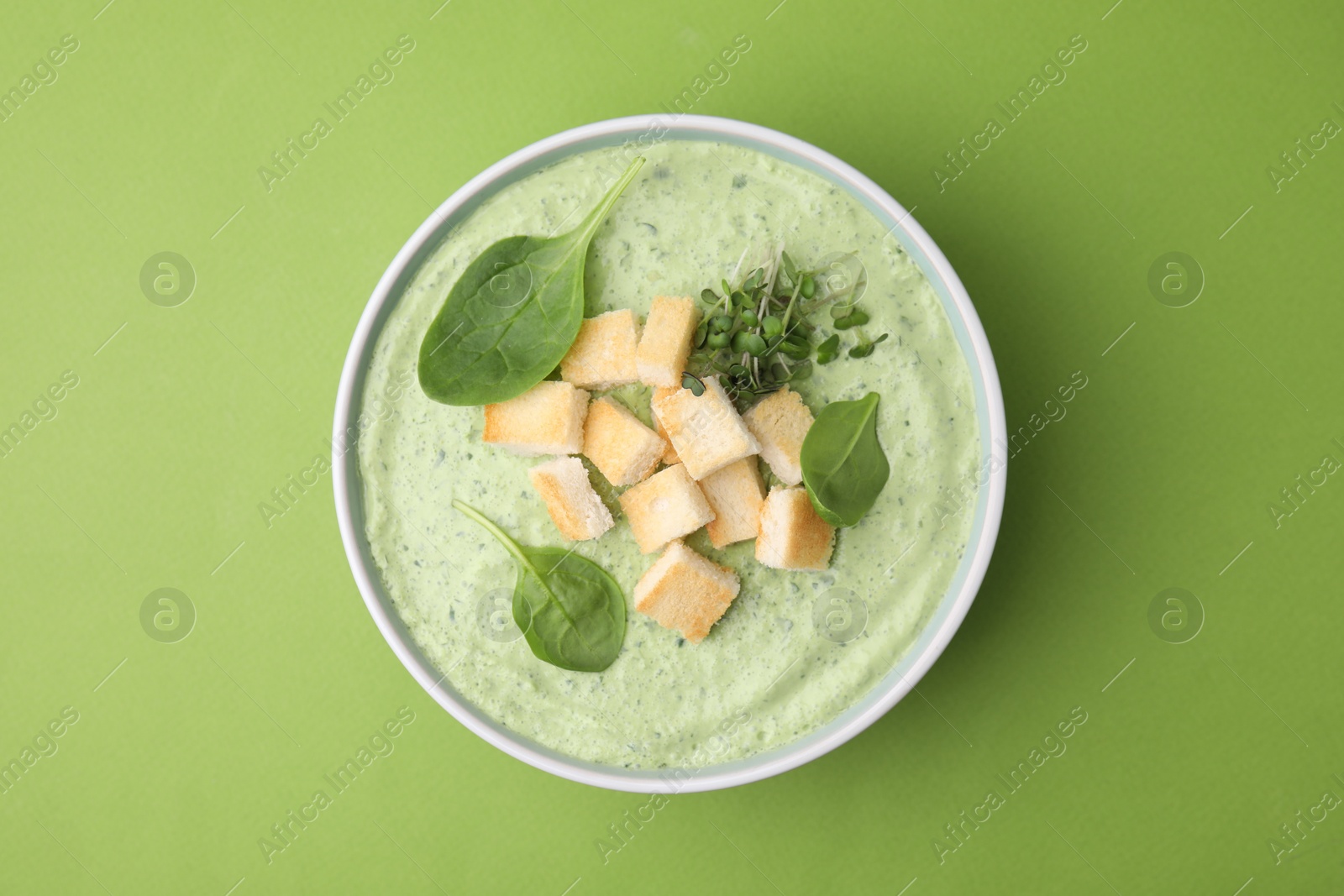 Photo of Delicious spinach cream soup with croutons in bowl on green background, top view