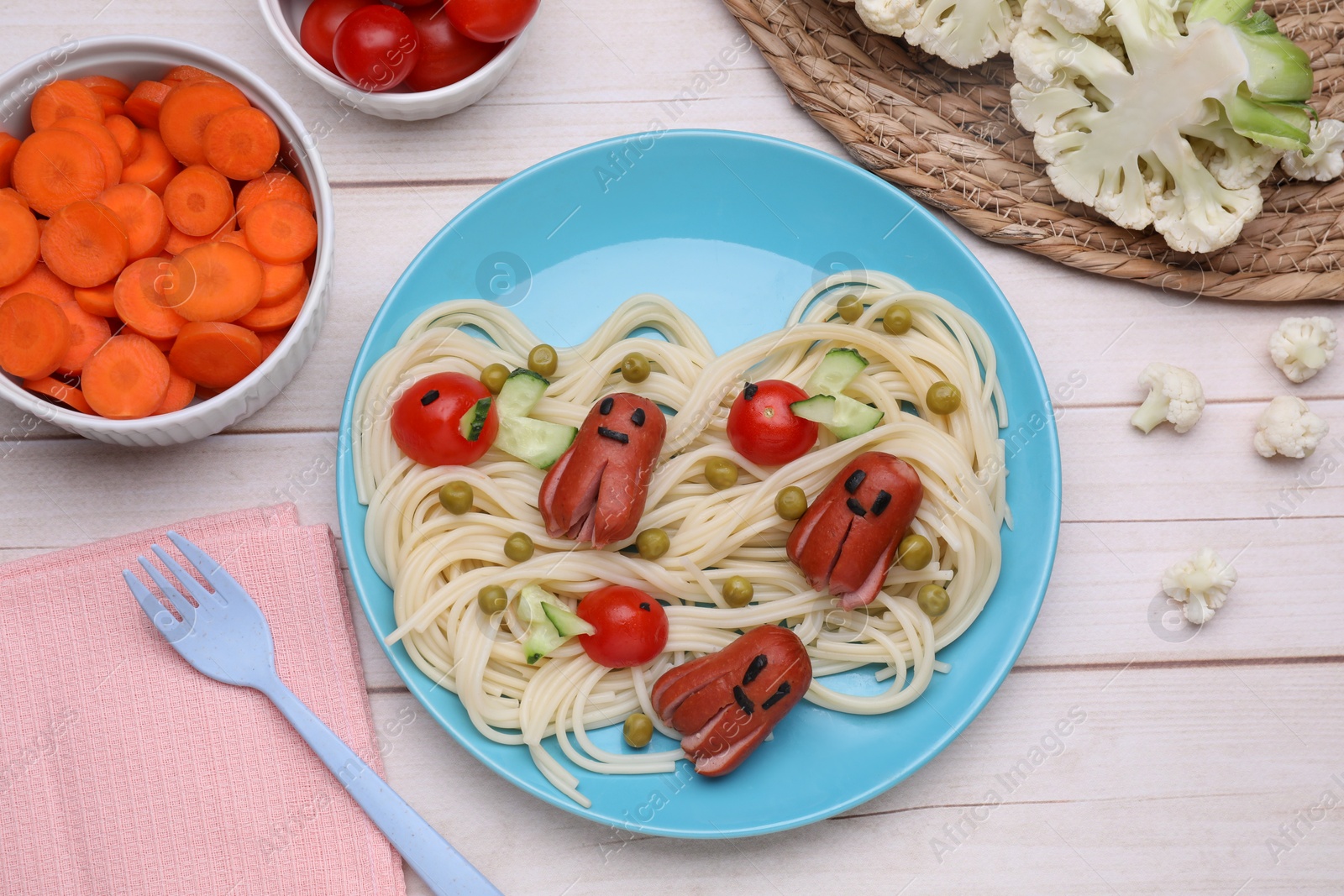 Photo of Creative serving for kids. Plate with cute octopuses made of sausages, pasta and vegetables on white wooden table, flat lay