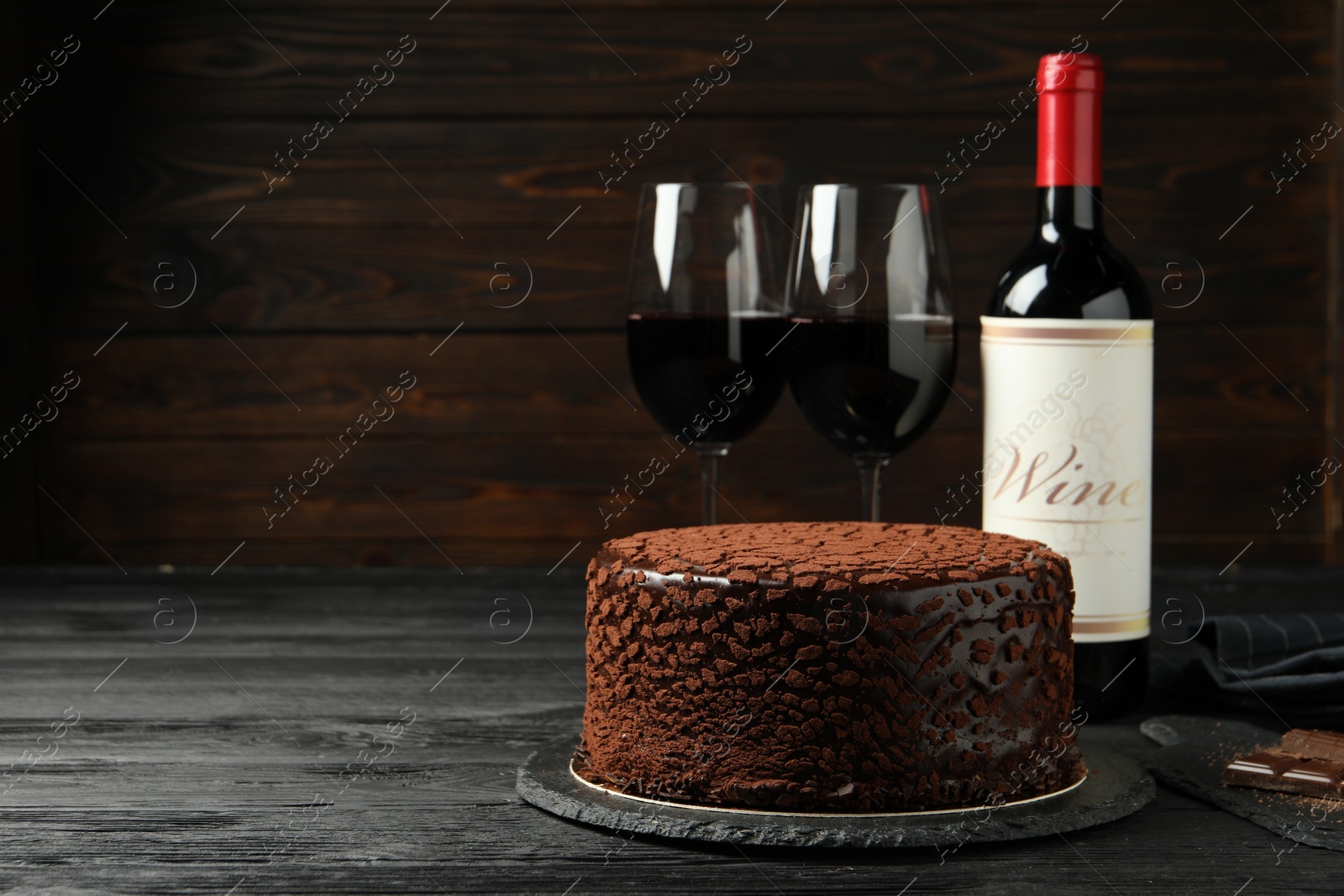 Photo of Delicious chocolate truffle cake and red wine on black wooden table, space for text