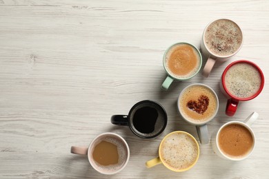 Photo of Many cups with different aromatic coffee on white wooden table, flat lay. Space for text