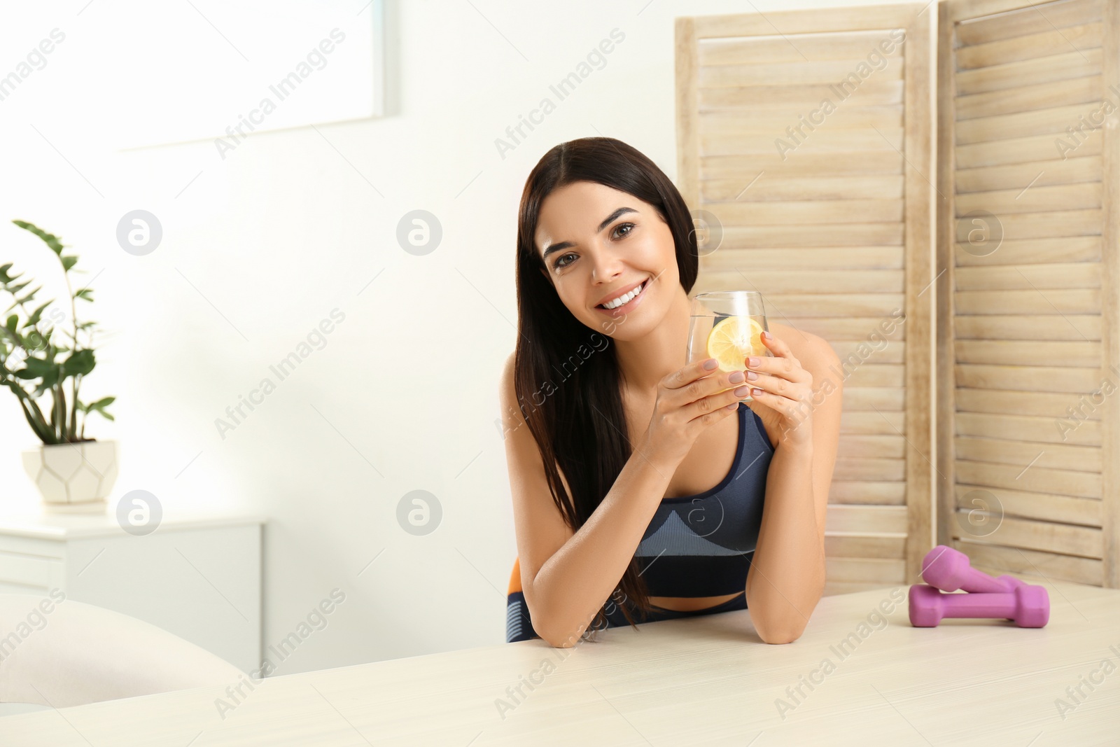 Photo of Beautiful sportive woman with lemon water at table indoors