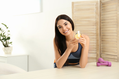Beautiful sportive woman with lemon water at table indoors