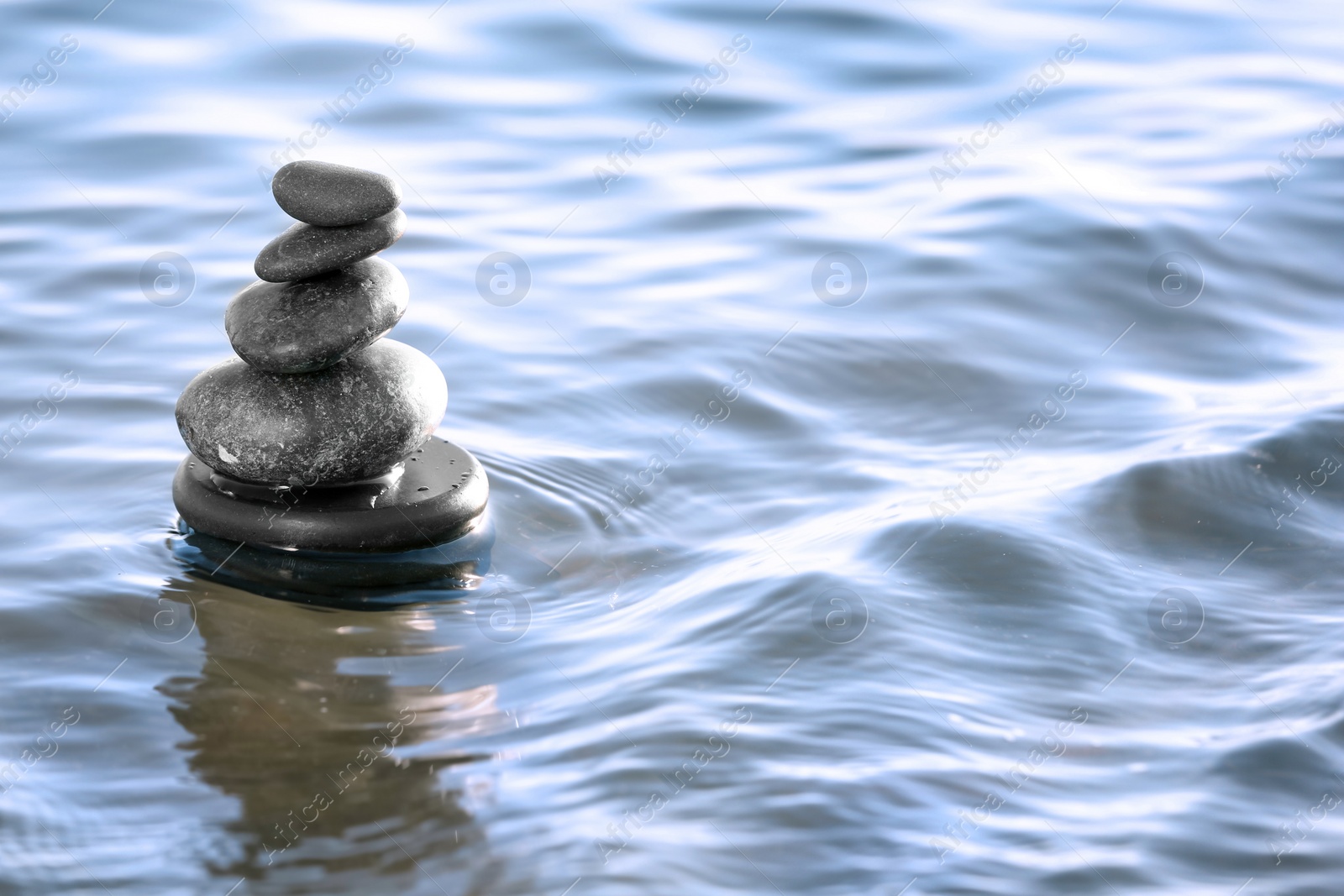 Photo of Stack of dark stones in sea water, space for text. Zen concept