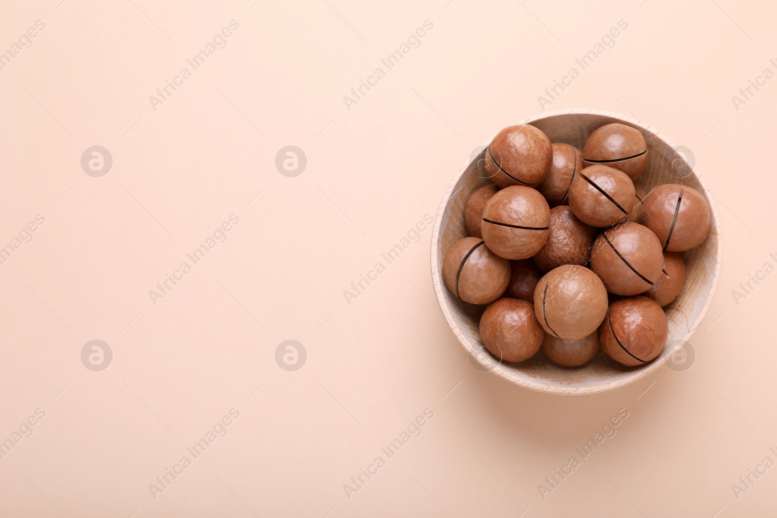 Photo of Delicious organic Macadamia nuts in wooden bowl on beige background, top view. Space for text