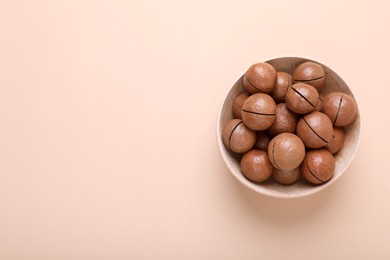 Photo of Delicious organic Macadamia nuts in wooden bowl on beige background, top view. Space for text