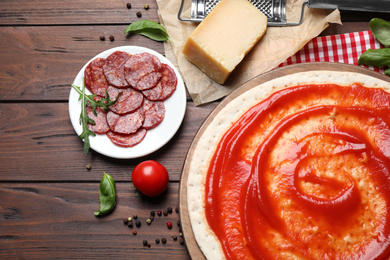 Photo of Flat lay composition with base and fresh ingredients for pepperoni pizza on wooden table