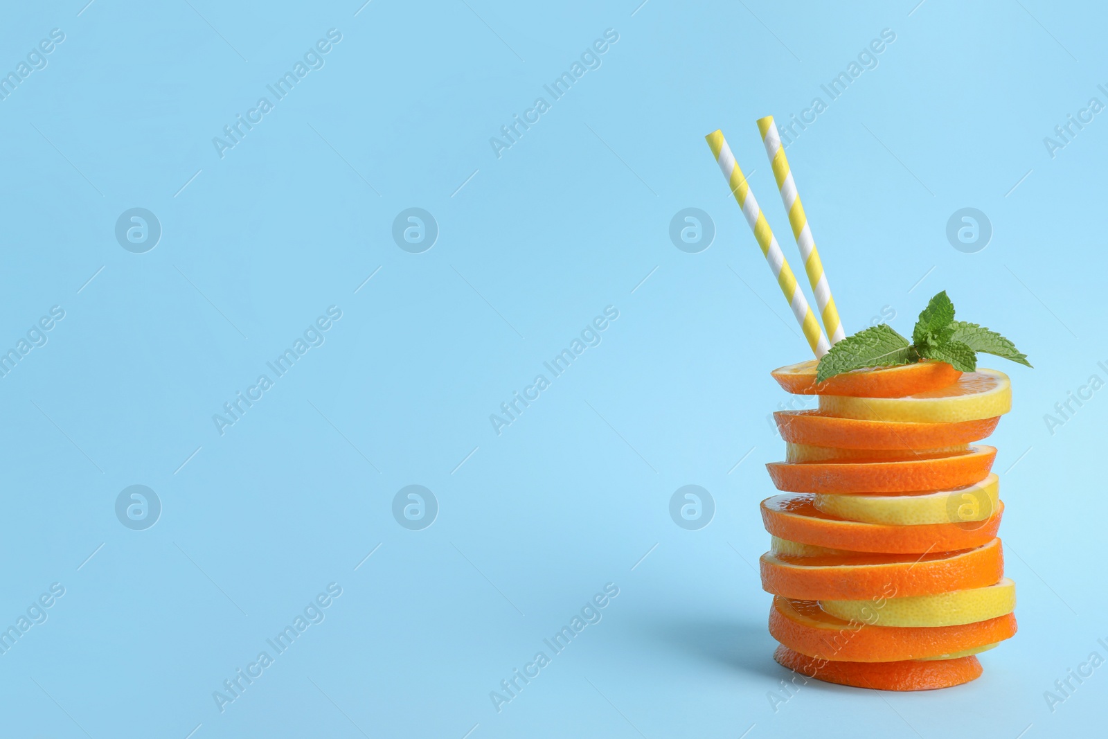 Photo of Stacked orange and lemon slices with straws as cocktail on light blue background. Space for text
