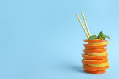 Stacked orange and lemon slices with straws as cocktail on light blue background. Space for text