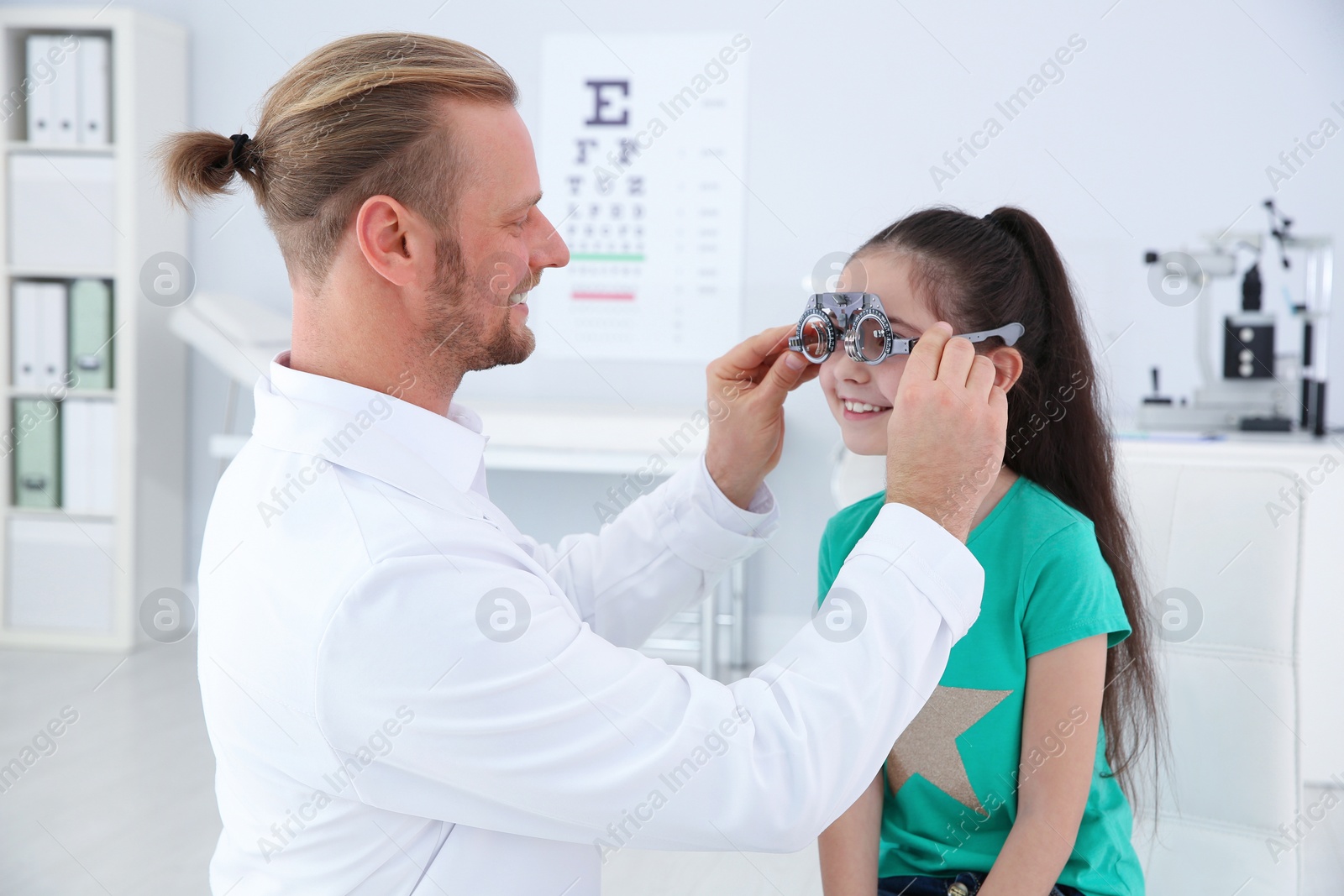 Photo of Children's doctor putting trial frame on little girl in clinic. Eye examination