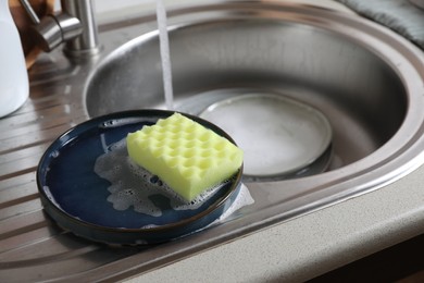 Photo of Plates and sponge in kitchen sink. Washing dishes