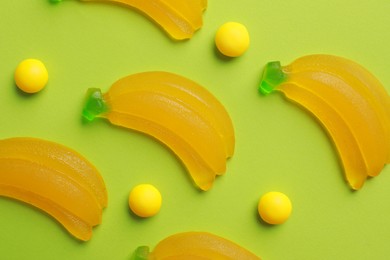 Delicious dragee and gummy banana candies on green background, flat lay
