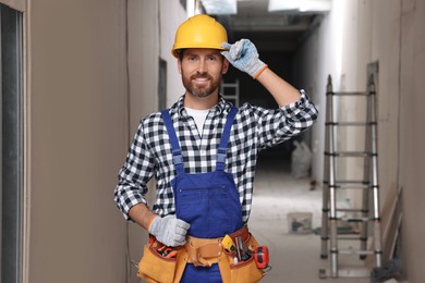 Professional builder in uniform with tool belt indoors