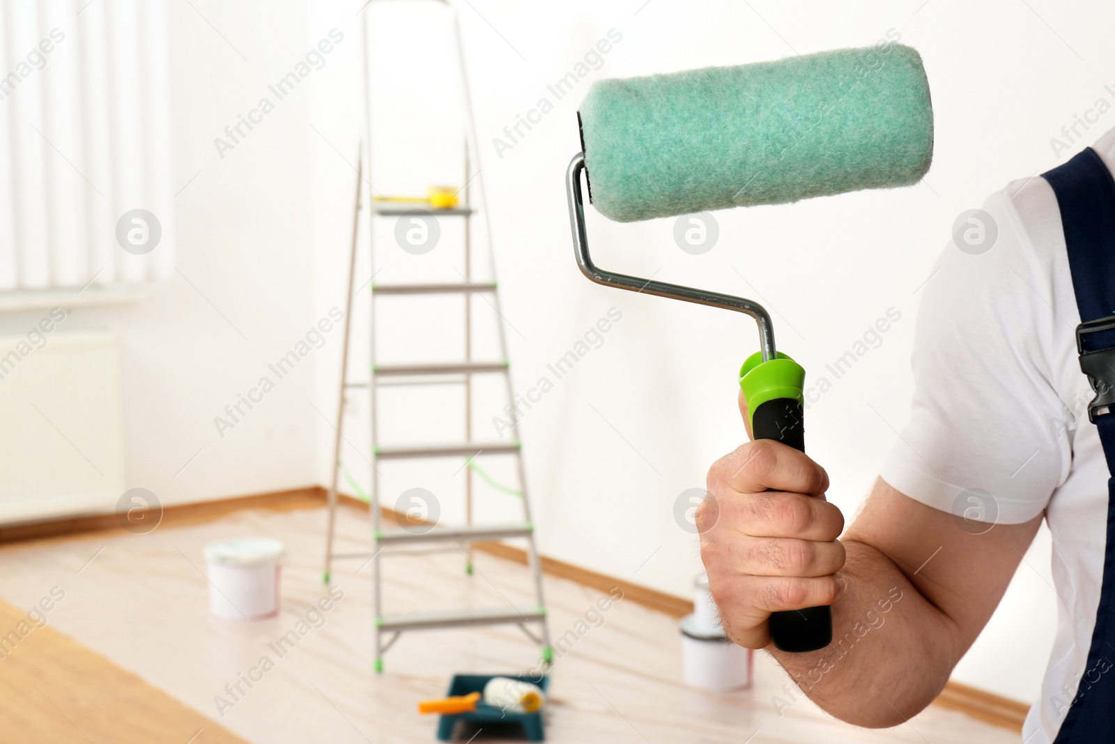 Photo of Male decorator with paint roller in empty room, closeup. Space for text