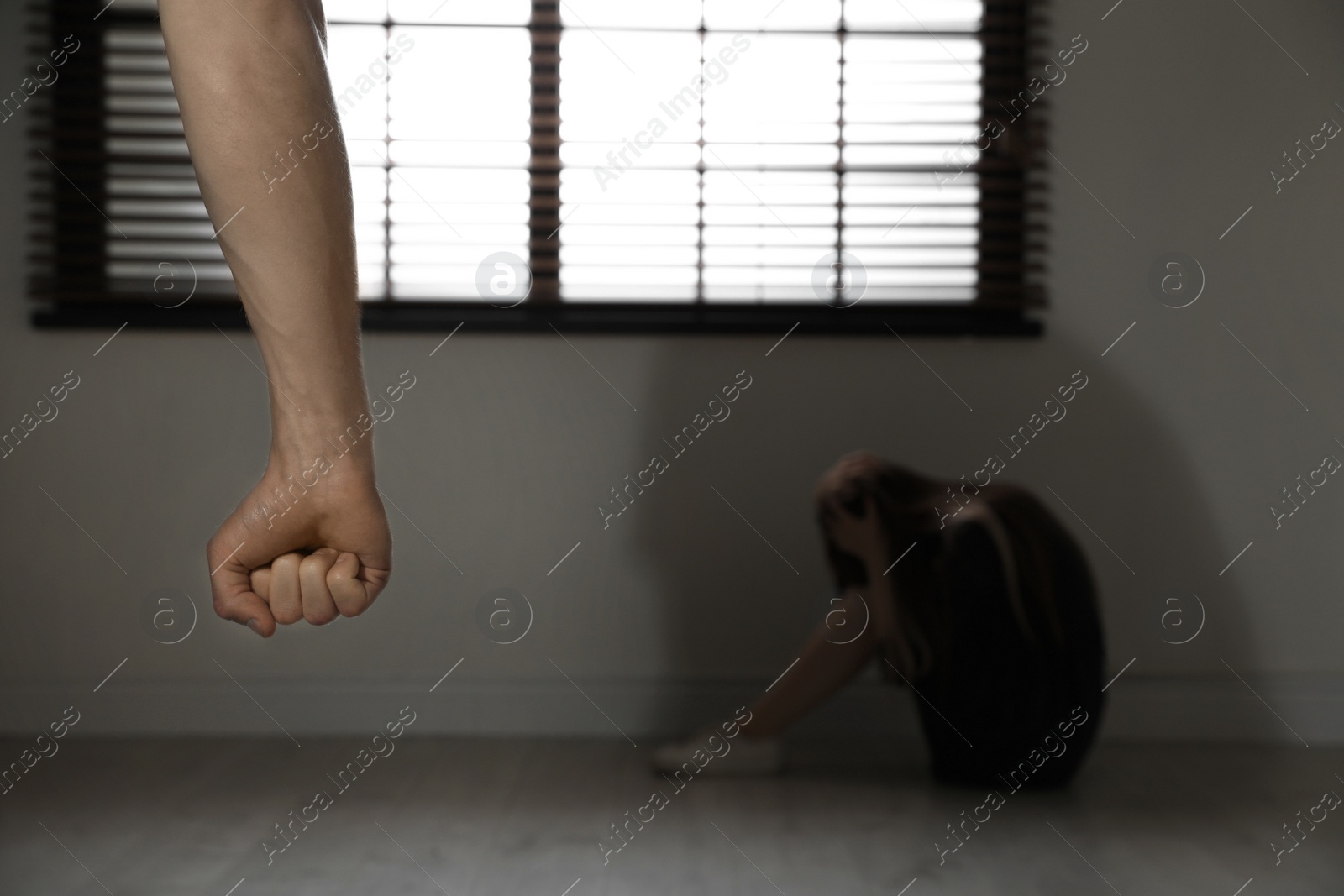 Photo of Closeup of man's fist and blurred woman indoors, space for text. Stop sexual assault