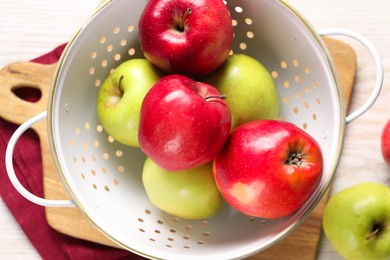 Photo of Fresh apples in colander on white wooden table, flat lay