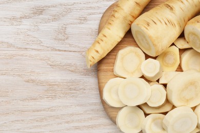 Photo of Whole and cut fresh ripe parsnips on white wooden table, top view. Space for text