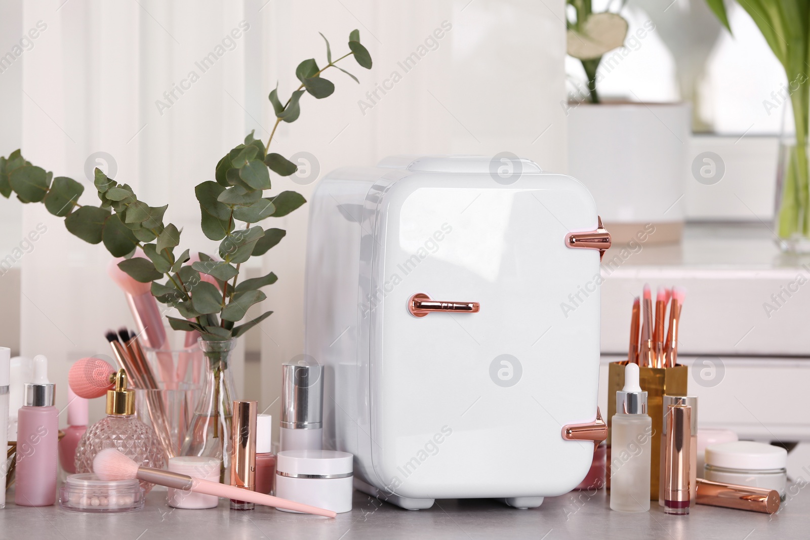 Photo of White mini cosmetics refrigerator and skin care products on table