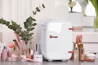 Photo of White mini cosmetics refrigerator and skin care products on table