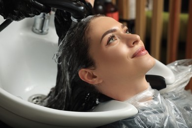 Photo of Hairdresser rinsing out dye from woman's hair in beauty salon