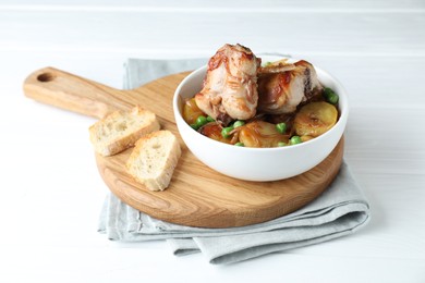 Tasty cooked rabbit with vegetables in bowl and bread on white wooden table