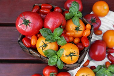 Photo of Different sorts of tomatoes with basil on wooden table, above view
