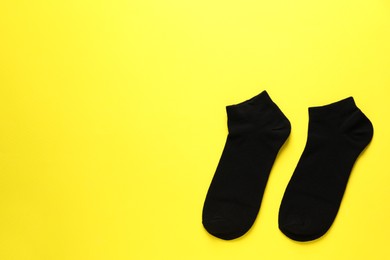 Pair of black socks on yellow background, flat lay. Space for text