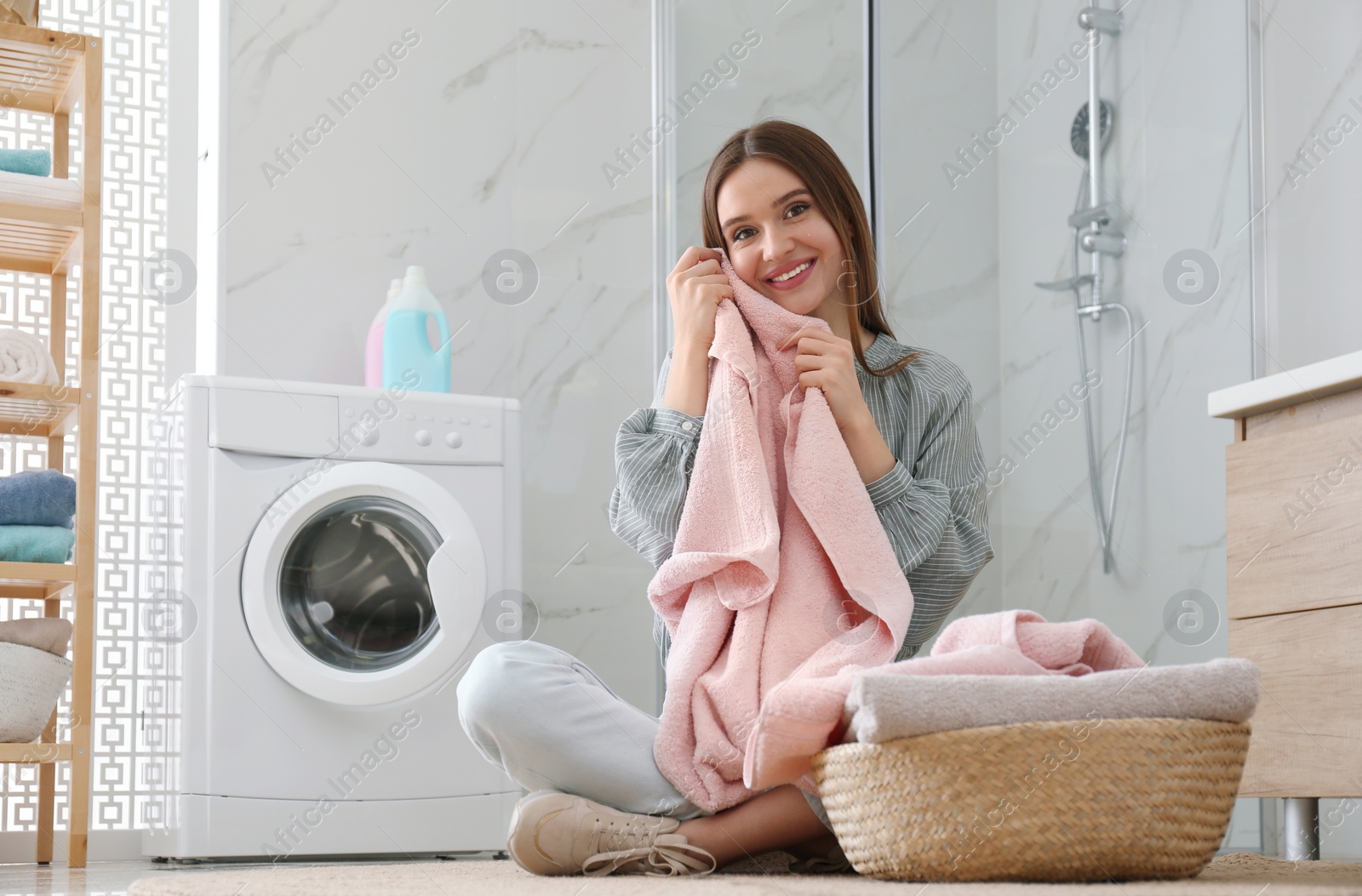 Photo of Happy woman with clean towel near washing machine in bathroom. Laundry day