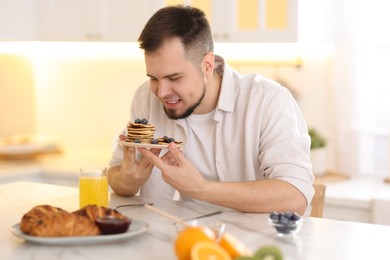Smiling man with plate of pancakes having tasty breakfast at home