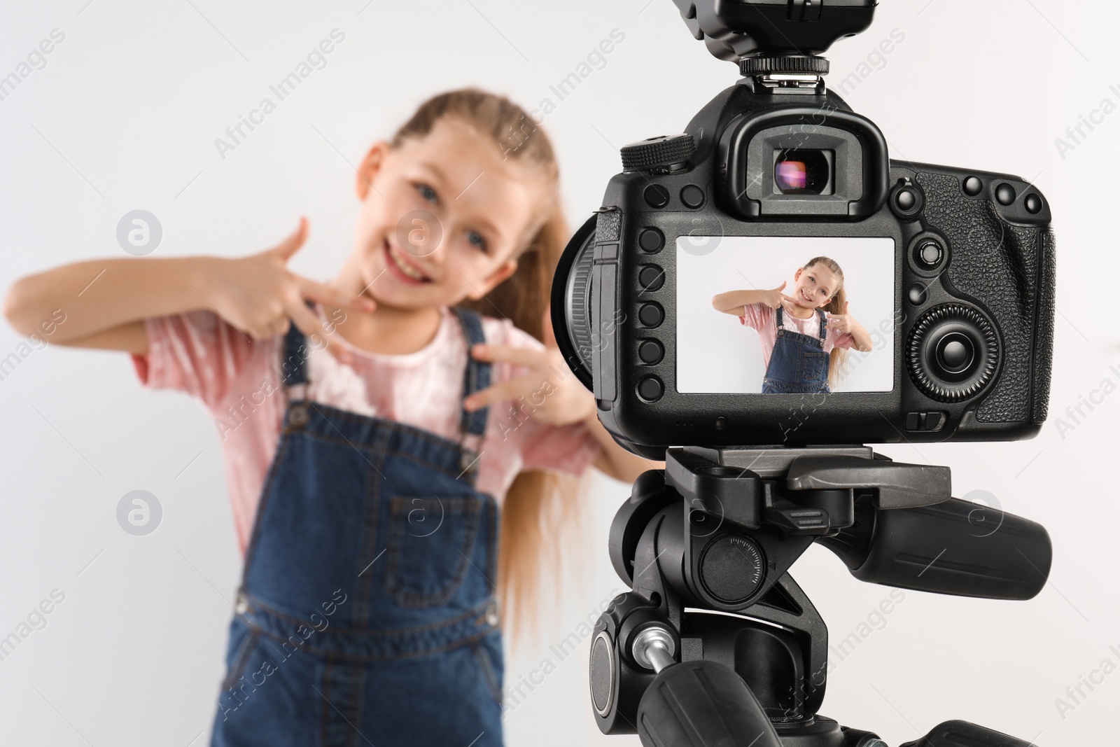 Photo of Cute little blogger recording video against white background, focus on camera