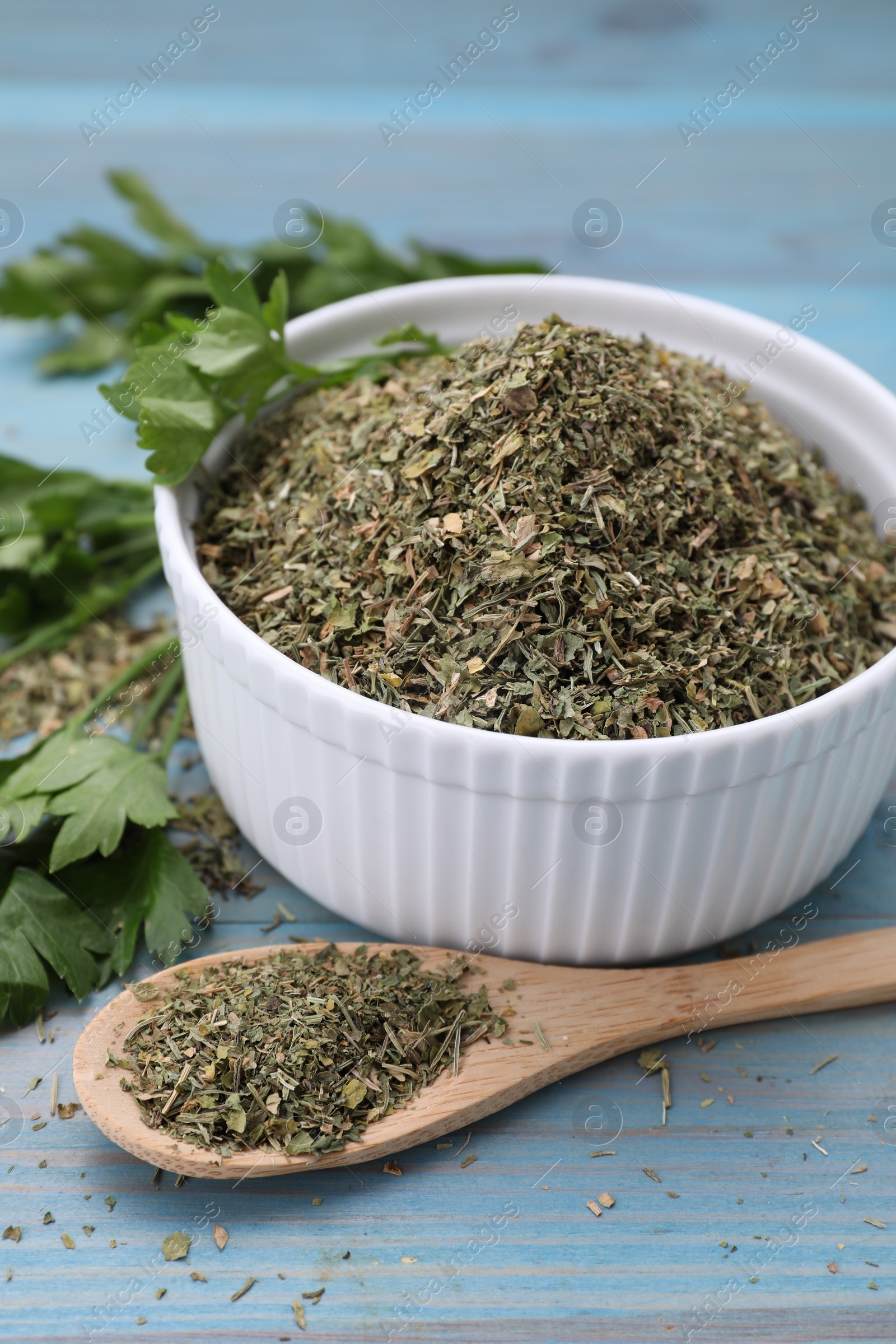 Photo of Dried parsley and fresh leaves on light blue wooden table, closeup