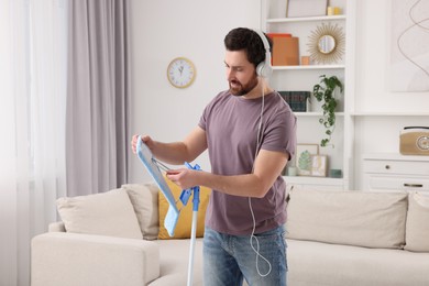 Photo of Spring cleaning. Man with headphones and mop in living room