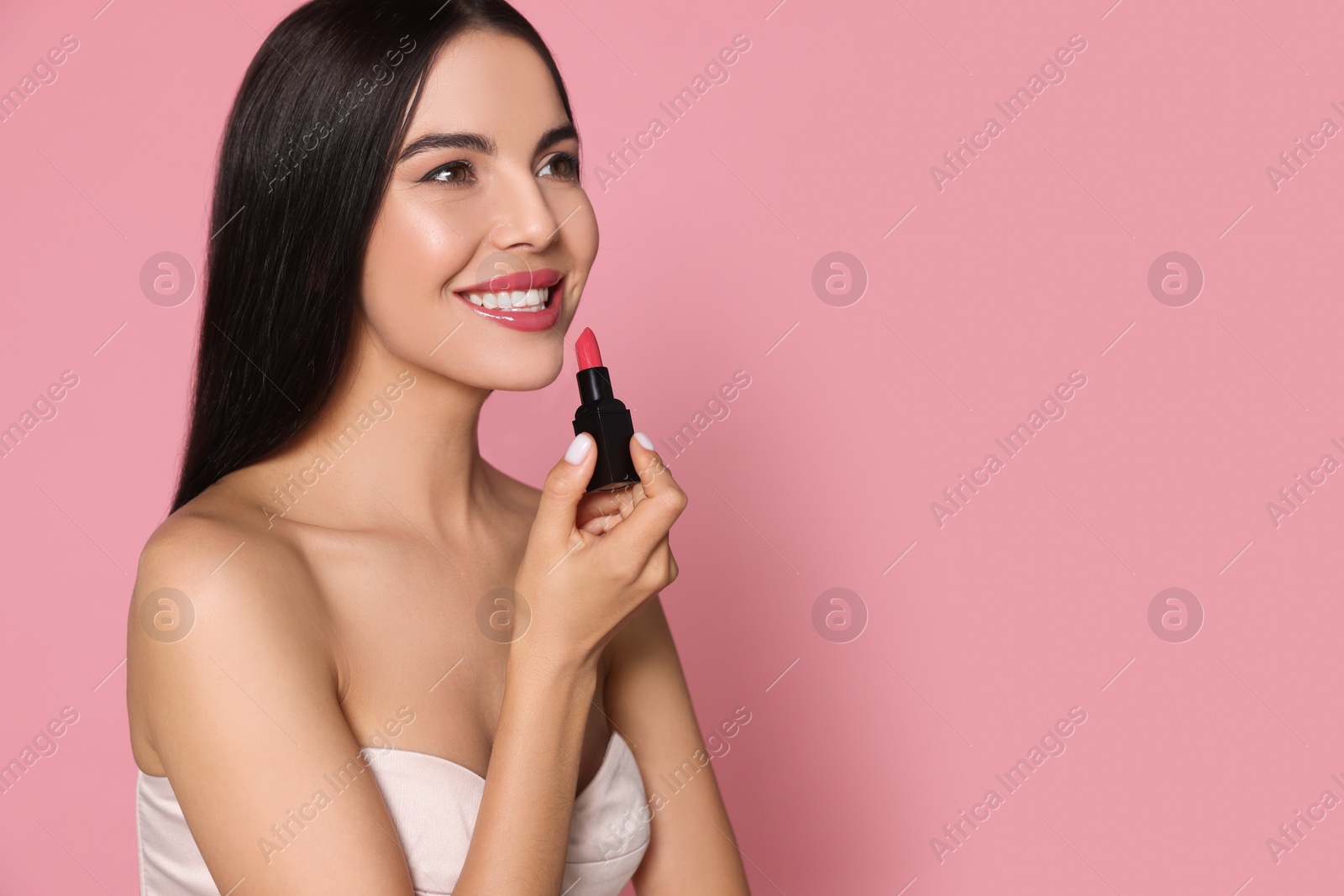 Photo of Young woman with beautiful makeup holding glossy lipstick on pink background, space for text