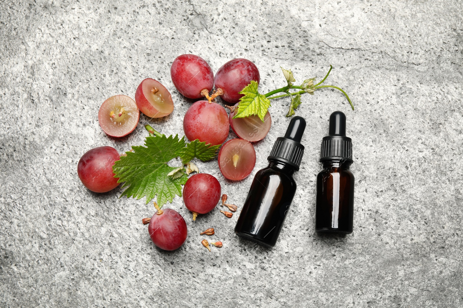 Photo of Bottles of natural grape seed oil on grey table, flat lay. Organic cosmetic