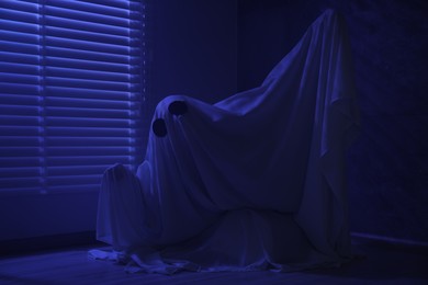 Creepy ghost. Woman covered with sheet near window in blue light