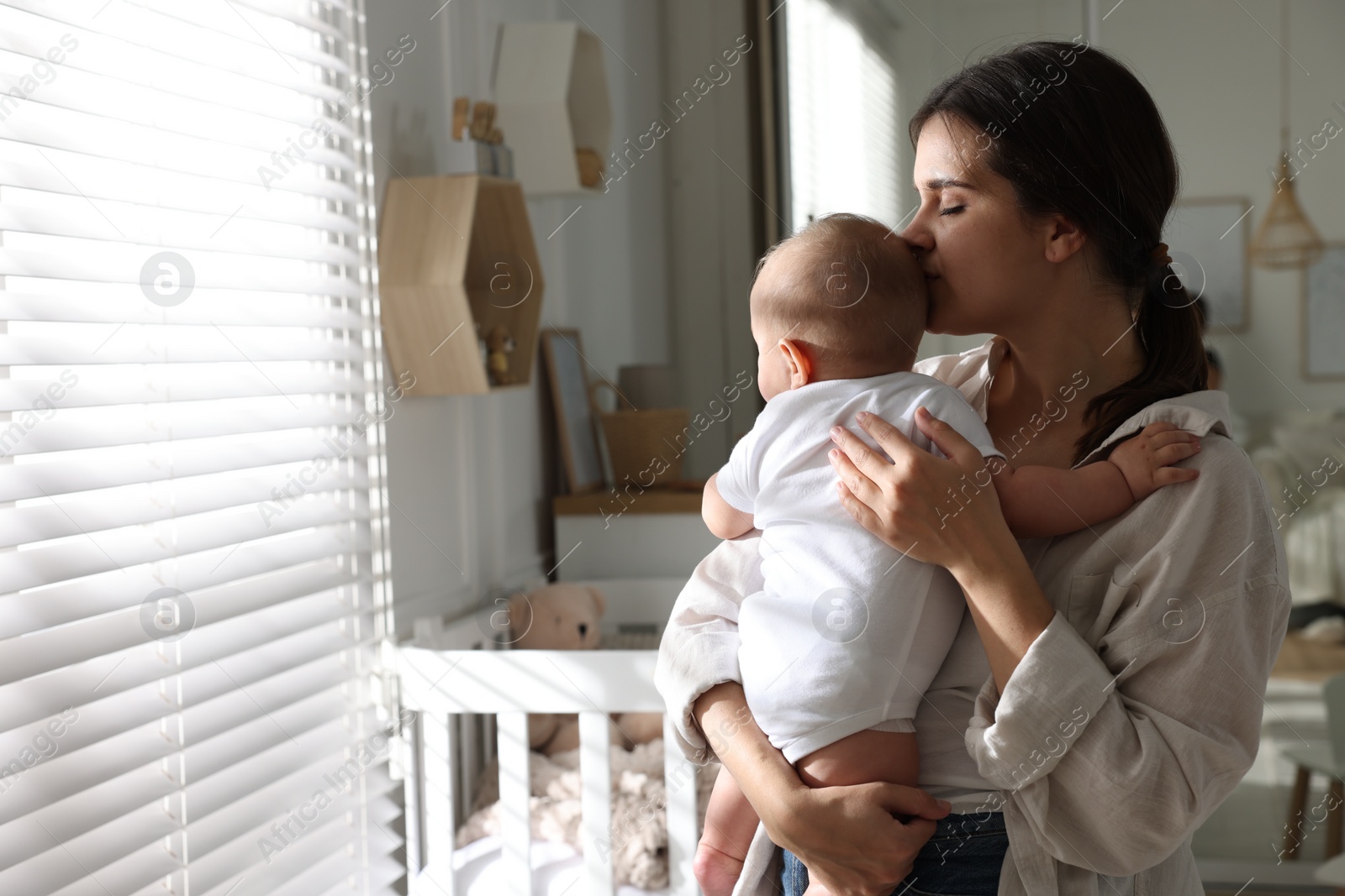 Photo of Young mother with her baby near window at home. Space for text