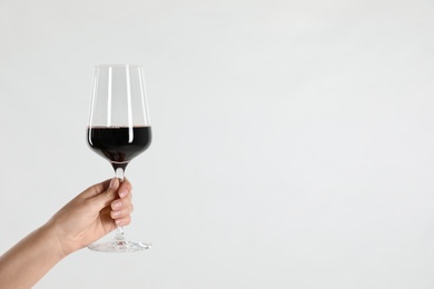 Woman holding glass of red wine on light background, closeup. Space for text